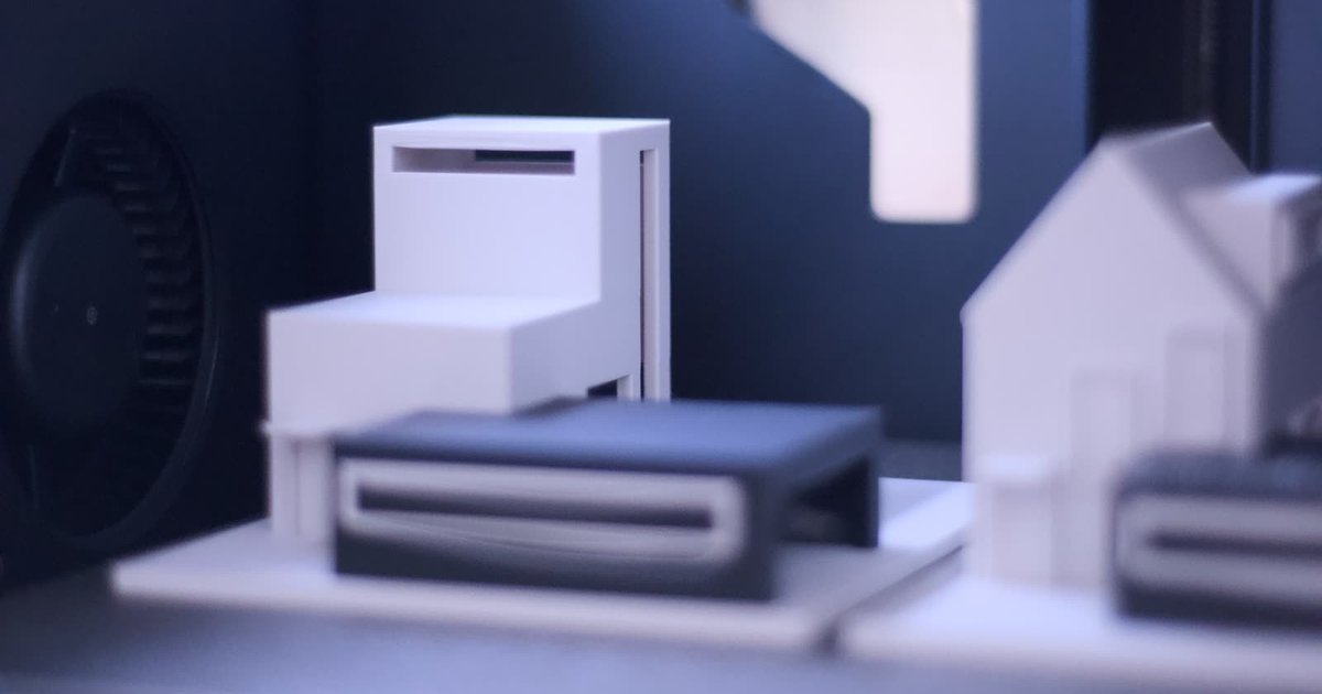 3D nyomtatott építészeti makett a nyomtató tálcáján: fehér lépcsőzött tömeg sötét földszinti résszel, telekalaplapon